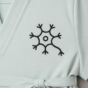 May include: A pale teal scrub top with a black embroidered neuron design. The top has a V-neck, short sleeves, and a matching tie belt. The neuron design is a stylized representation of a nerve cell.