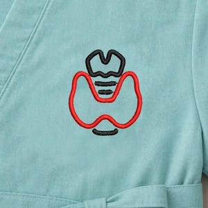 May include: A light teal scrub top with a black and red embroidered thyroid gland design. The medical-themed top features a V-neck and a tie at the waist. The embroidered design is centered on the chest.