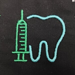 Può includere: Tessuto nero con un disegno ricamato raffigurante una siringa verde e un dente blu. La siringa è verticale e il dente è a destra. Il disegno è probabilmente legato all'odontoiatria o all'assistenza sanitaria.