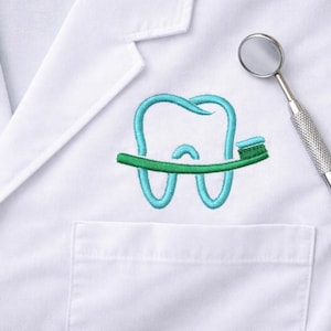 May include: A white lab coat with a teal embroidered tooth and toothbrush design. A dental mirror is positioned to the right of the design. The embroidered tooth has a blue outline and a white filling. The toothbrush is green.