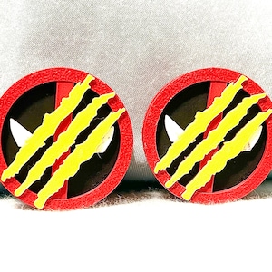 May include: Pair of round red and black earrings with yellow claw marks. Each earring features a white shape and a red border. The earrings are set against a light blue background.