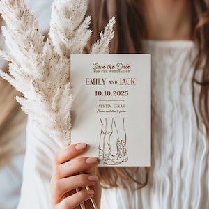 Może przedstawiać: Kremowa karta zaproszenia ślubnego z napisem "Save the Date" i imionami "Emily and Jack" w kolorze brązowym. Wyświetlana jest data "10.10.2025". Karta zawiera rysunek dwóch par nóg i kowbojskich butów.