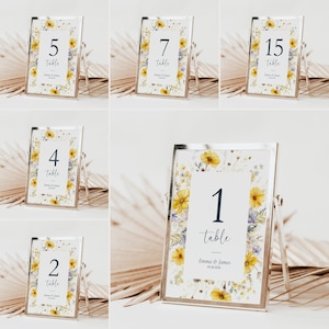 Puede incluir: Un conjunto de tarjetas con números de mesa en marcos plateados. Cada tarjeta muestra un número y la palabra «mesa» en fuente oscura. Las tarjetas están adornadas con un borde floral de flores amarillas y moradas.