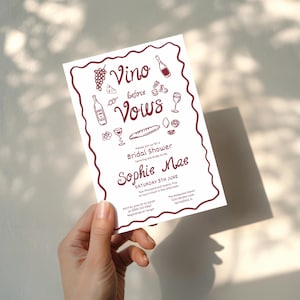 May include: A white invitation with a burgundy border and text. The invitation reads "Vino before Vows" with illustrations of wine bottles, grapes, and cheese. It announces a bridal shower for Sophie Mae on June 5th.