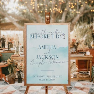 May include: A blue and white watercolor sign with the text "Something Blue Before I Do" and a diamond ring icon. The sign also includes the names "Amelia and Jackson" and the text "Couple Shower". The date "Saturday 15th of June" and the location "Miami Florida" are also included on the sign.