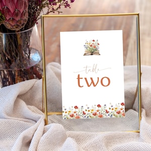 5x7" Un nuovo capitolo inizia numeri di tabella segno / libro di fiabe a tema / fiori di campo primaverili colorati / pila di libri aperti modello modificabile Canva