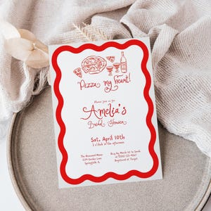 May include: A white invitation with a red wavy border and red text. The text reads "Pizza my heart!" and "Amelia's Bridal Shower" with the date and time. Pizza and wine illustrations are at the top.
