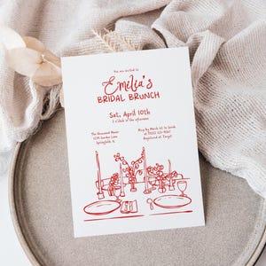 May include: A white invitation card with red text and illustrations for a bridal brunch. The text reads "Emilia's Bridal Brunch" and includes the date, time, and location. The illustration depicts a table setting with candles and floral arrangements.