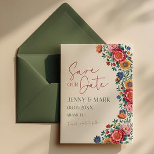 Pode incluir: Um convite de casamento com o texto "Save Our Date" em escrita bordô, rodeado por uma borda floral de flores rosa, vermelhas, amarelas e azuis. O convite está em um fundo creme, com um envelope verde.