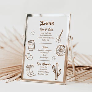 May include: A silver framed bar menu with a white background. The menu features the text "The BAR" and lists beer, cider, wine, and non-alcoholic beverages. Illustrations of a guitar, barrel, and cactus are included.