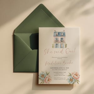 Peut inclure: Une invitation pour une fête prénuptiale avec une illustration d'un bâtiment parisien. L'invitation dit "She said Oui!" et comprend les détails de l'événement, des motifs floraux et une enveloppe verte.