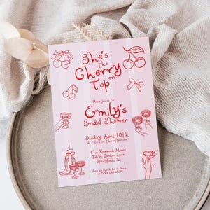 May include: Pink and white striped bridal shower invitation with red text that reads "She's the Cherry on Top" and "Emily's Bridal Shower". The invitation includes details about the date, time, location, and RSVP information.