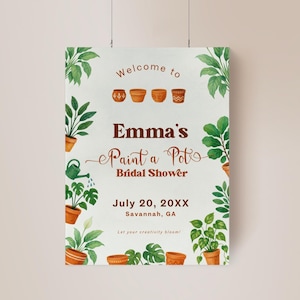 May include: A decorative sign for a bridal shower, with the text "Emma's Paint a Pot" in brown script. The sign includes illustrations of potted plants and the date July 20, 20XX, in Savannah, GA. The sign is surrounded by green foliage.