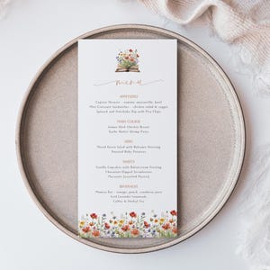 May include: A printable menu template with a floral design. The menu features a book with flowers on top and the word "menu" written in cursive. The menu lists appetizers, main course, sides, sweets, and beverages.