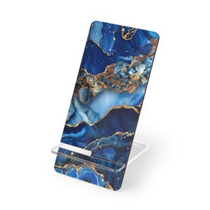 May include: A phone stand with a blue and gold abstract design. The stand has a rectangular top with a marbled pattern of deep blues and gold accents. The stand is supported by a clear, angled base.