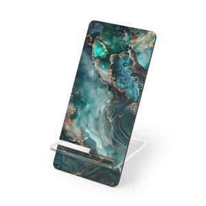 Puede incluir: Un soporte decorativo para teléfono con un diseño abstracto vibrante. El soporte presenta un patrón arremolinado de color turquesa, verde y dorado, que se asemeja al mármol o al ágata. El soporte es de acrílico transparente.