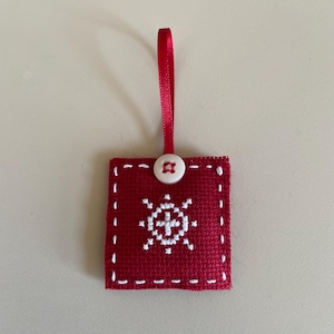 May include: A red fabric ornament with a white snowflake design and a white button. The ornament has a red ribbon for hanging.