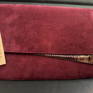 May include: A burgundy suede clutch with a snakeskin flap and a gold label that says "Faith".
