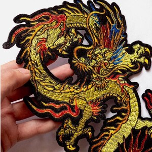 Könnte beinhalten: Gestickter Drachenaufnäher in Gold, Rot und Blau. Das Drachendesign weist komplizierte Details und einen schwarzen Rand auf. Geeignet für Jacken, Taschen oder andere Stoffartikel.