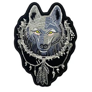 Op de afbeelding: Geborduurde strijkpatch met het hoofd van een grijze wolf met gele ogen, omringd door een zwart-wit droomvangerontwerp.
