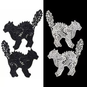 Peut inclure: Deux appliques en dentelle, noires et blanches, en forme de chats. Les chats sont détaillés avec des motifs complexes et ont un style fantaisiste et décoratif.