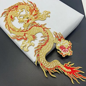 Peut inclure: Patch brodé représentant un dragon doré et rouge. Le dragon est enroulé sur lui-même, la queue dans la gueule. Le patch est détaillé avec des paillettes et a un contour blanc.