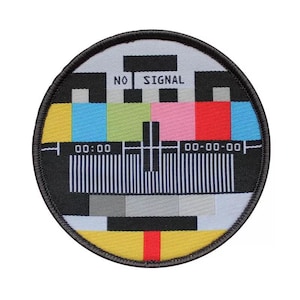 Peut inclure: Un patch rond noir et blanc avec un motif d'essai de télévision coloré. Le motif comprend une série de barres colorées, une grille noir et blanc et le texte "NO SIGNAL" au centre. Le patch a une bordure noire.