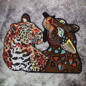 Può includere: Due toppe ricamate di leopardi, una marrone e una arancione e bianca, con paillettes e dettagli colorati.