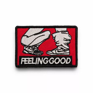 Könnte beinhalten: Ein gestickter Patch in Rot und Schwarz mit zwei Cartoon-Beinen, die Turnschuhe tragen. Der Text "Feeling Good" ist in Weiß auf einem schwarzen Banner gedruckt.