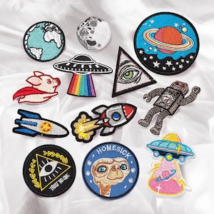 Può includere: Un set di 12 toppe da stirare con diversi design, tra cui un pianeta, un UFO, un maiale, un robot, un occhio, un razzo, una creatura del film E.T. e un triangolo con un occhio. Le toppe sono tutte colorate e hanno una varietà di stili.