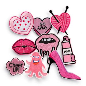Könnte beinhalten: Ein Set mit rosa Bügelbildern mit verschiedenen Designs, darunter ein Herz mit Punkten, ein Herz mit dem Text "Go Away", ein Paar Lippen, ein tropfender Mund, ein rosa Tintenfisch, eine Sprechblase mit dem Text "Cheer Up!" ein rosa High-Heel-Schuh, eine Tube rosa Farbe mit dem Text "Pink" und ein Herz mit Nadel und Garn.