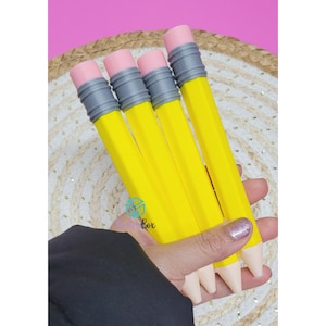Puede incluir: Cuatro bolígrafos amarillos diseñados para parecer lápices de madera tradicionales, cada uno con una virola de color gris metálico y una punta de goma rosa. Los bolígrafos tienen un cuerpo amarillo brillante y una punta cónica blanquecina.