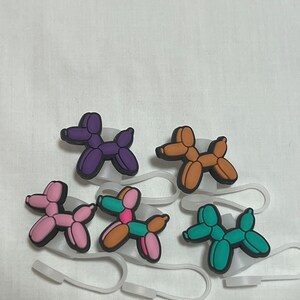 May include: Five balloon animal charms in different colors: purple, brown, pink, brown and teal. The charms are shaped like dogs and are attached to clear plastic rings.