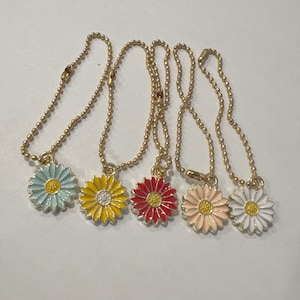 May include: Five gold chain necklaces with colorful daisy charms. The charms are blue, yellow, red, pink, and white.