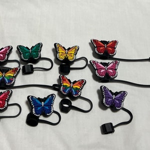 May include: Assortment of colorful butterfly phone charms with black elastic straps. Each charm features a different butterfly design with rhinestones.