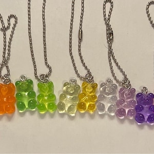 May include: A set of 12 gummy bear necklaces with silver chains. The gummy bears are in various colors, including clear, blue, orange, green, yellow, purple, red, and pink.