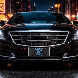 May include: A black luxury car with bright headlights and a license plate that reads "WHAT UP DOE!". The car is parked on a wet street at night, with city lights reflecting in the wet road surface.