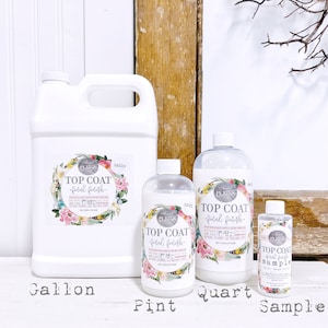 May include: Four bottles of white satin top coat paint in different sizes: a gallon, a quart, a pint, and a sample size. The bottles are labeled "Top Coat - Final Finish" with a floral design.