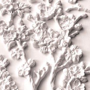 May include: White floral branch decorations with detailed blossoms and buds. The three-dimensional, relief-style design features multiple branches with flowers and leaves. The decorative elements are arranged on a white background.