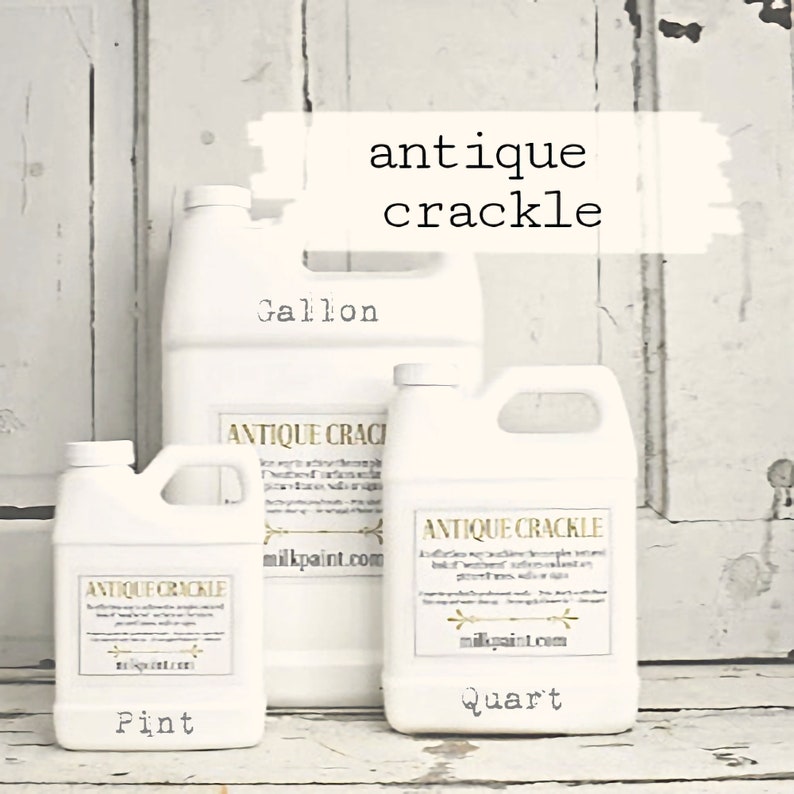 May include: Three white plastic bottles of antique crackle paint in pint, quart, and gallon sizes. The bottles are labelled with the product name and the size. The bottles are sitting on a white wooden surface.