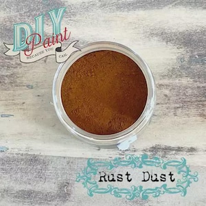 May include: A clear jar filled with rust-colored powder, labeled "Rust Dust." The jar sits on a weathered, light-colored wooden surface. The text "DIY Paint Because You Can" is in the upper left corner.