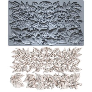 May include: A gray silicone mold featuring intricate botanical designs of leaves, berries, and nuts, paired with a white cast showing the finished relief. The mold includes text labels indicating capacities of 52ml, 38ml, and 7.4ml, plus Hazel & Bay IOD.