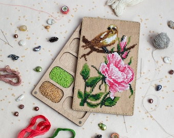 May include: A wooden box with compartments for beads and a hinged lid with a beaded embroidery of a bird perched on a branch with a pink rose.