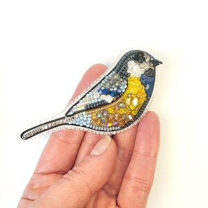 a hand holding a small bird brooch in it's left hand