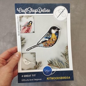 A hand holding a kit for creating a bird embroidery piece, with images of the kit and a bird embroidery design.