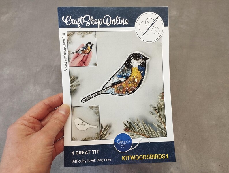 A hand holding a kit for creating a bird embroidery piece, with images of the kit and a bird embroidery design.