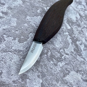 May include: A small, curved, wooden-handled knife with a silver blade. The blade is engraved with the word "FHURBA".