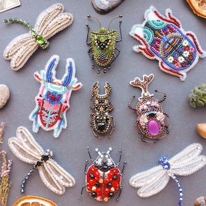 a collection of nine intricately designed, colorful, and detailed insect brooches or badges, each with unique patterns and embellishments.