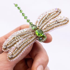 A hand holding a decorative piece of jewelry featuring a green gemstone and intricate beading.