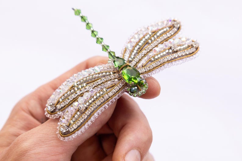 A hand holding a decorative piece of jewelry featuring a green gemstone and intricate beading.